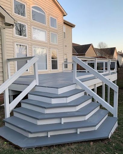 A deck with stairs and a railing in front of a house.