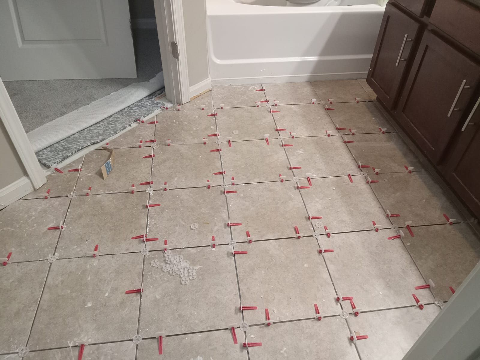 Bathroom floor with beige tiles being installed, red tile leveling clips present.