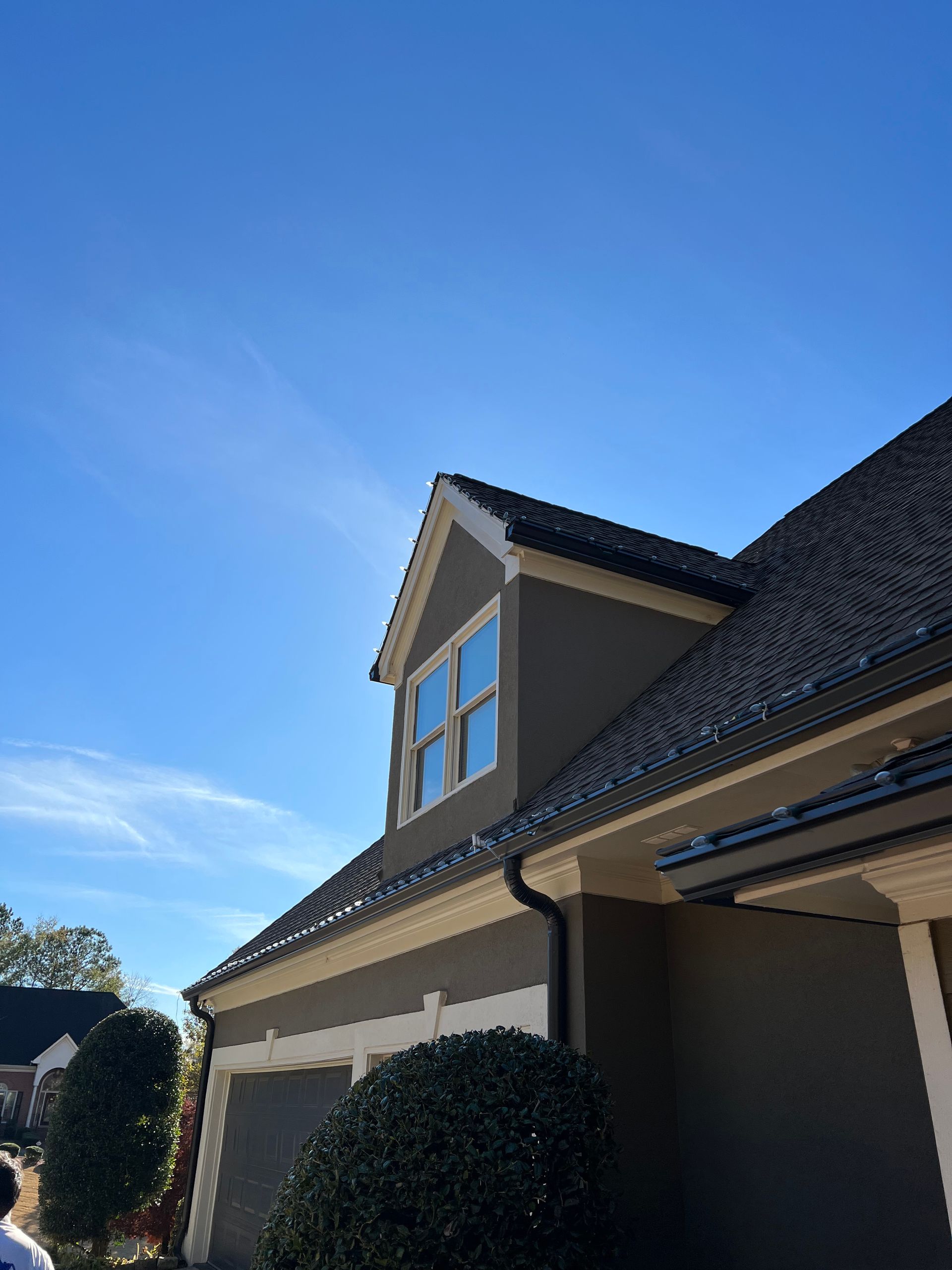 House exterior with gray stucco, black roof, and dormer under a blue sky.