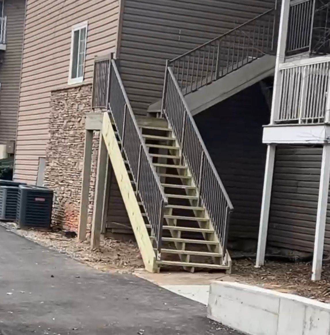 Wooden outdoor staircase leading up to a building's second floor. Brown siding and metal railings.