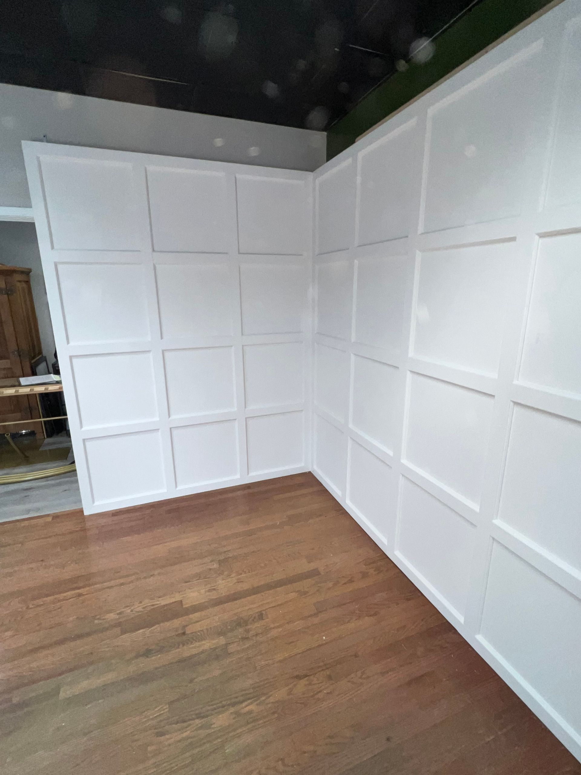 White paneled walls in a corner of a room with a hardwood floor.