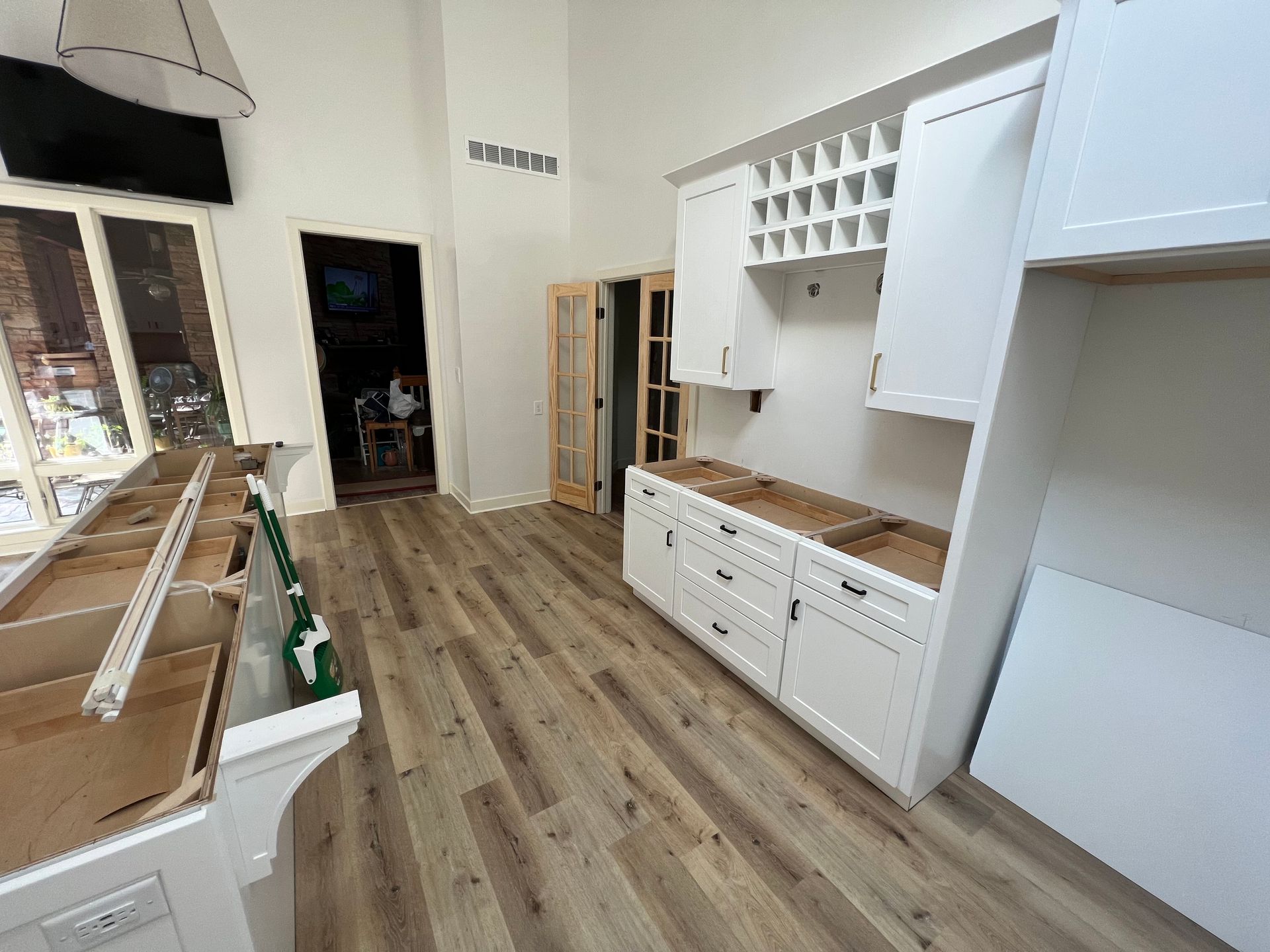 Kitchen under renovation with white cabinets, wood flooring, and a wine rack.