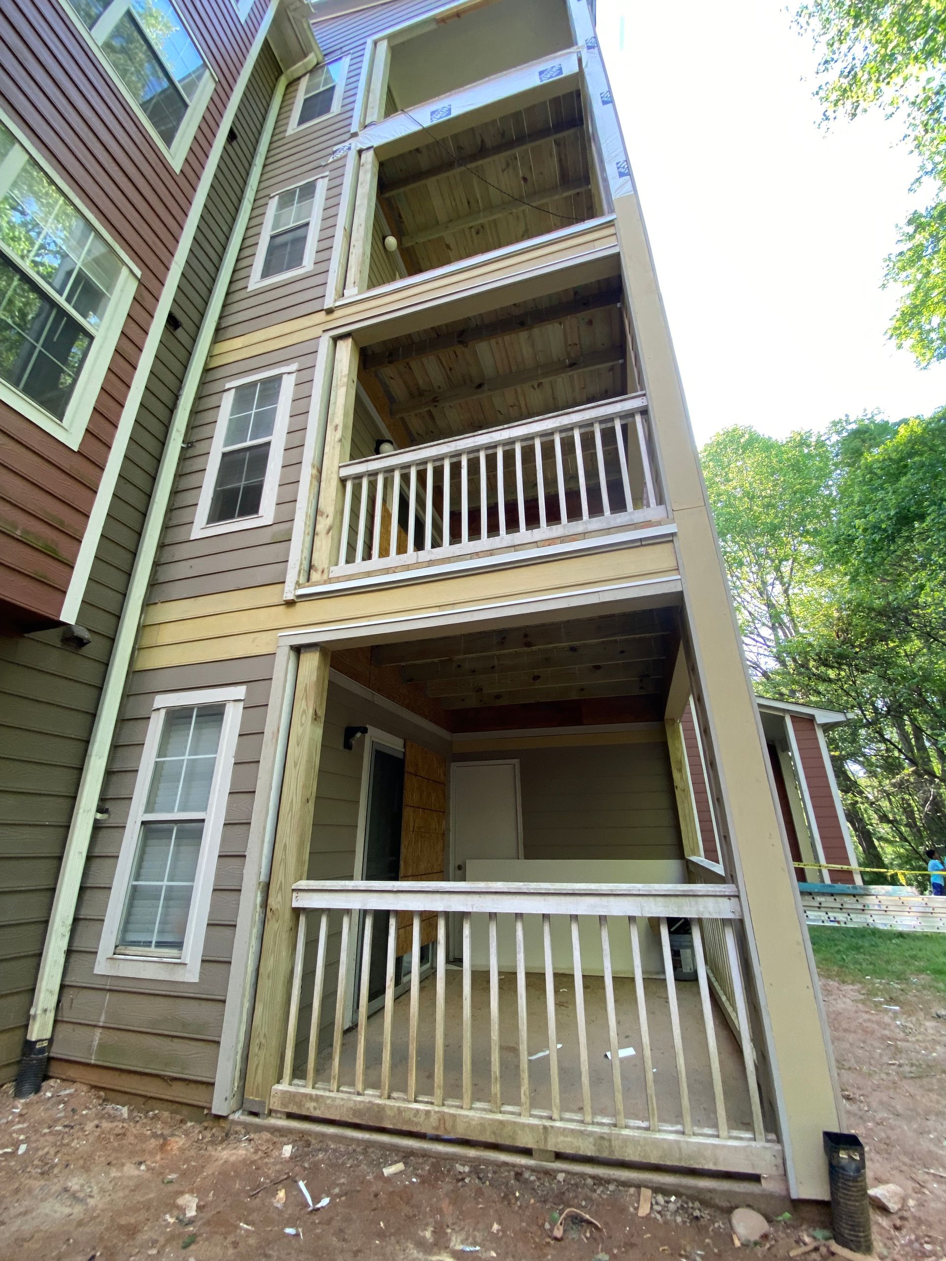 Multi-story building with several wooden balconies, beige siding, and surrounding trees.