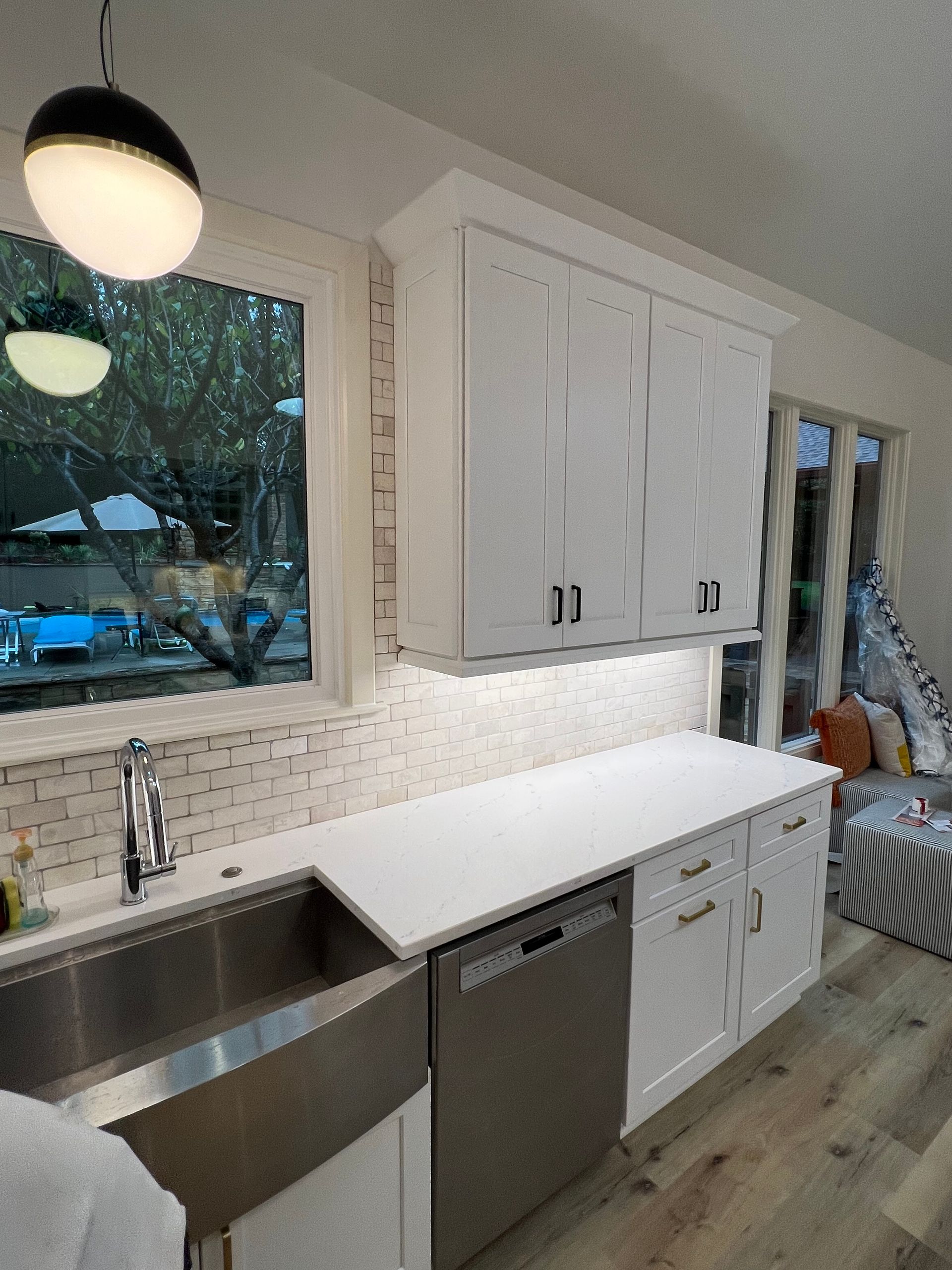 White kitchen cabinets, stainless steel sink, and dishwasher under a window, bright interior.