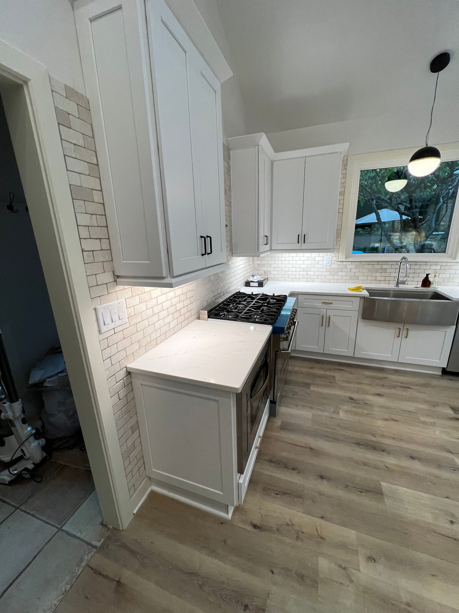 White kitchen with cabinets, stove, sink, and wood-look flooring. Window over sink.