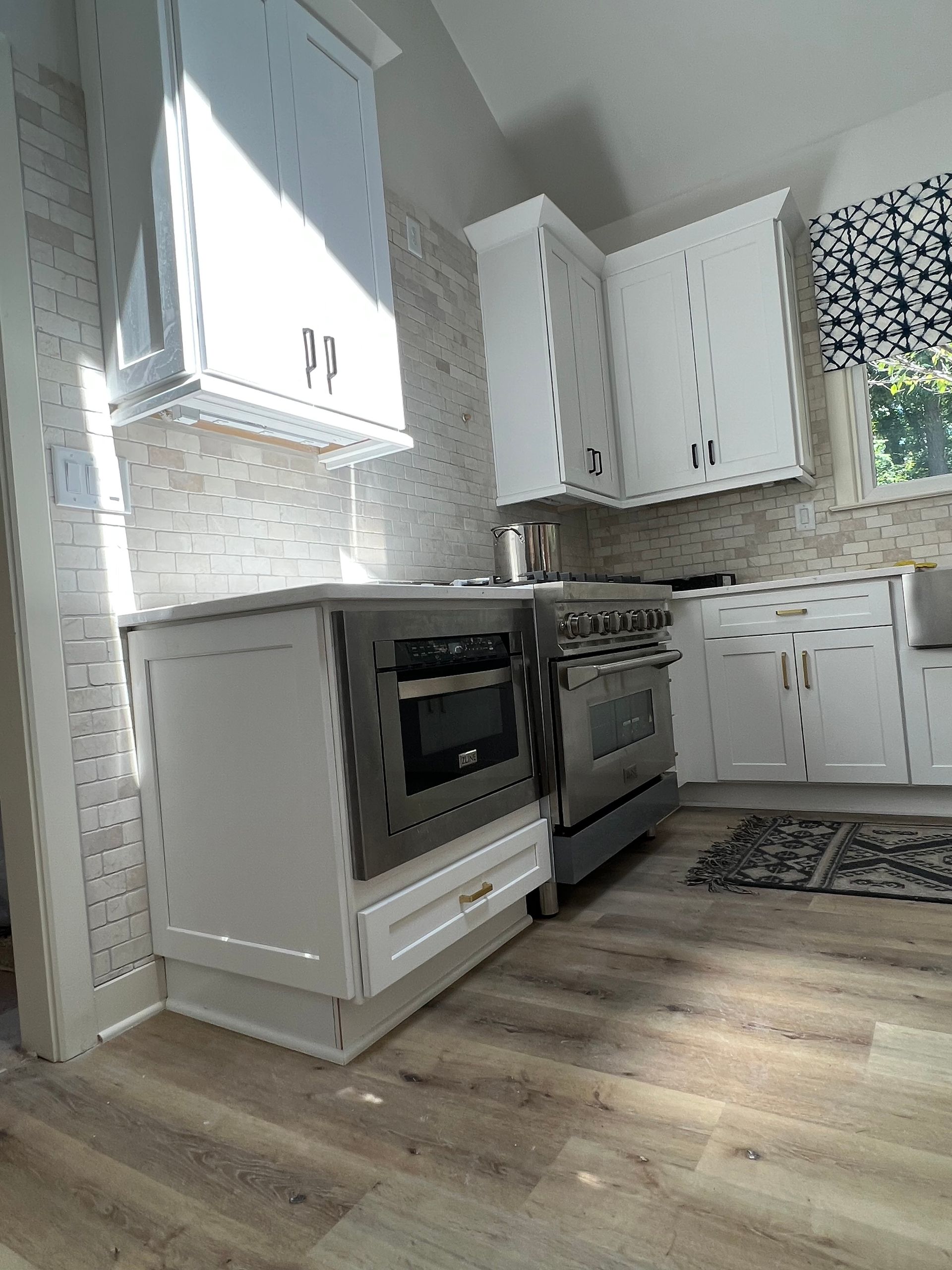 White kitchen cabinets and stainless steel appliances against a light brick tile backsplash.