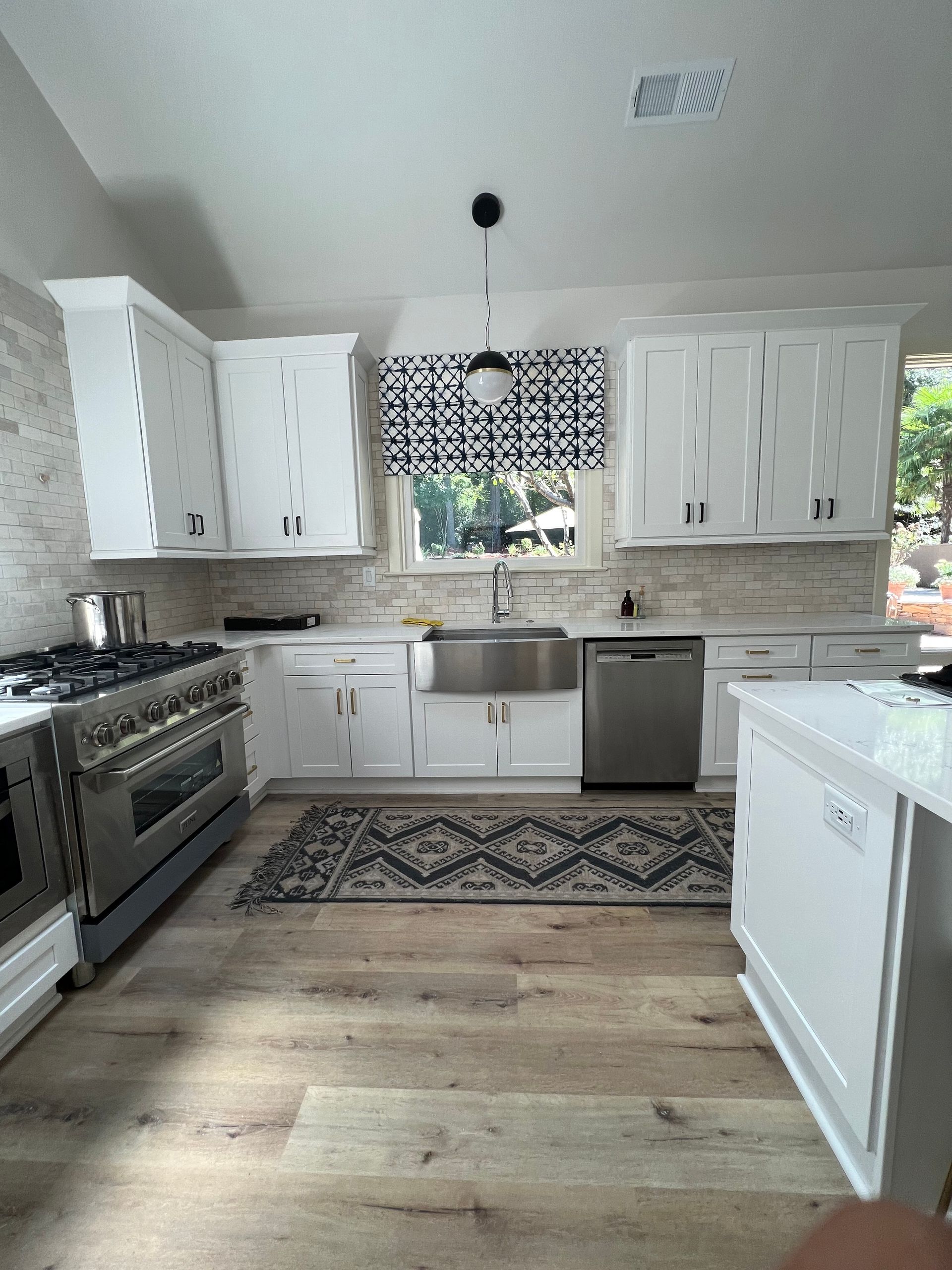 White kitchen with stainless steel appliances, white cabinets, and patterned rug.