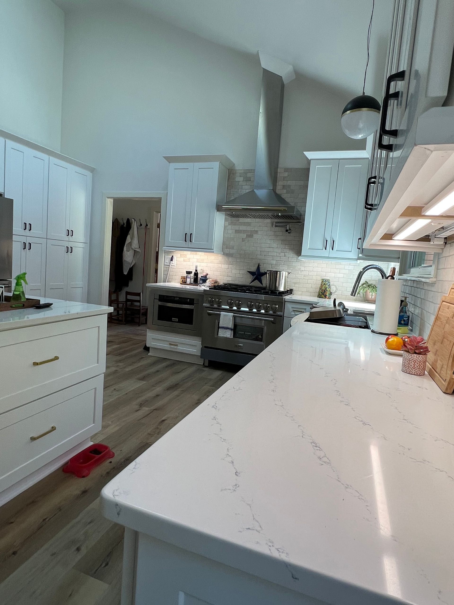 Bright, modern kitchen with white cabinets, light countertops, stainless steel appliances, and wood flooring.