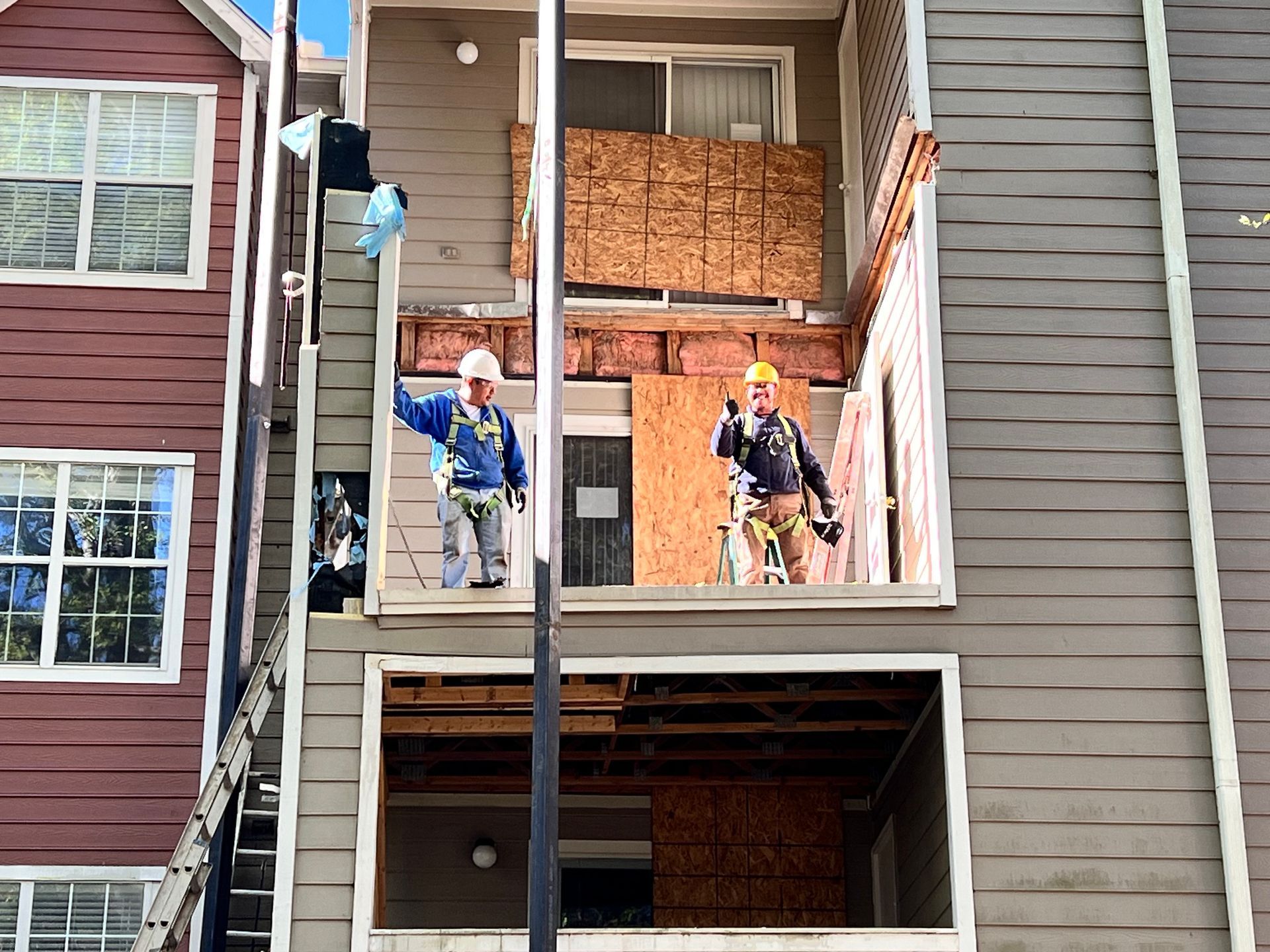 Two construction workers on scaffolding, repairing a multi-story apartment building exterior.