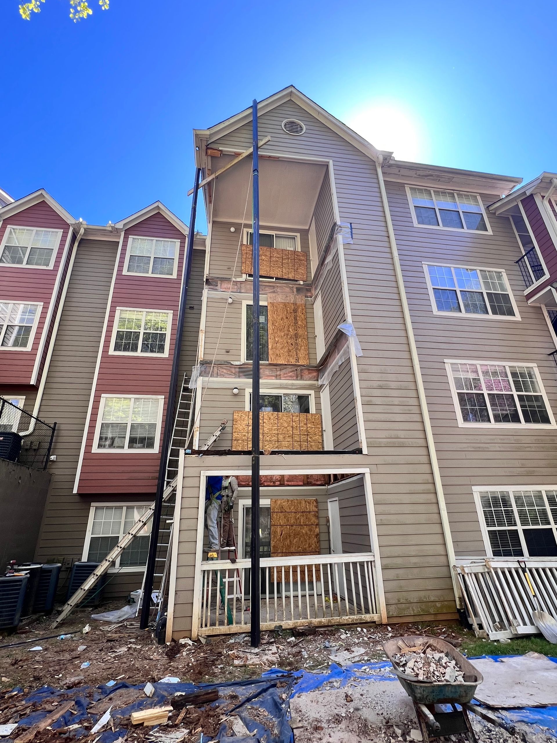 Apartment building exterior undergoing construction; boarded up windows and balconies; clear sky.