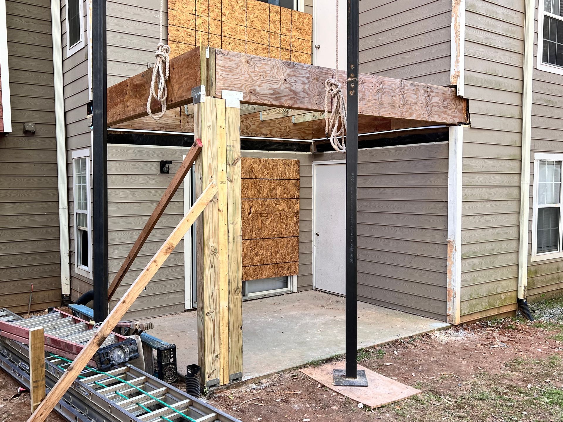 Apartment exterior under construction; porch area with unfinished wood framing, support beams, and a concrete patio.