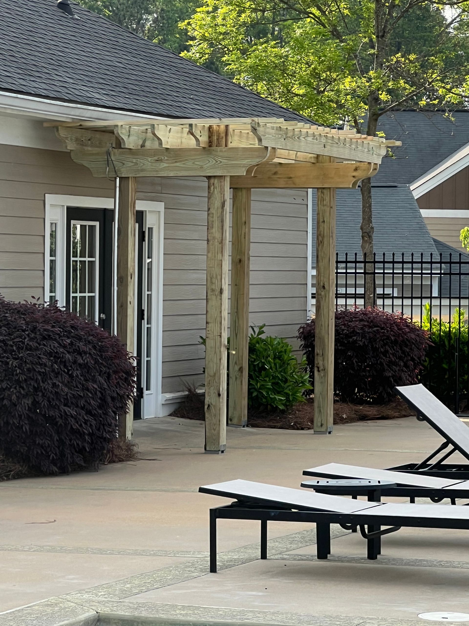 Poolside pavilion with stone roof, supported by wooden posts. Loungers are in the foreground.