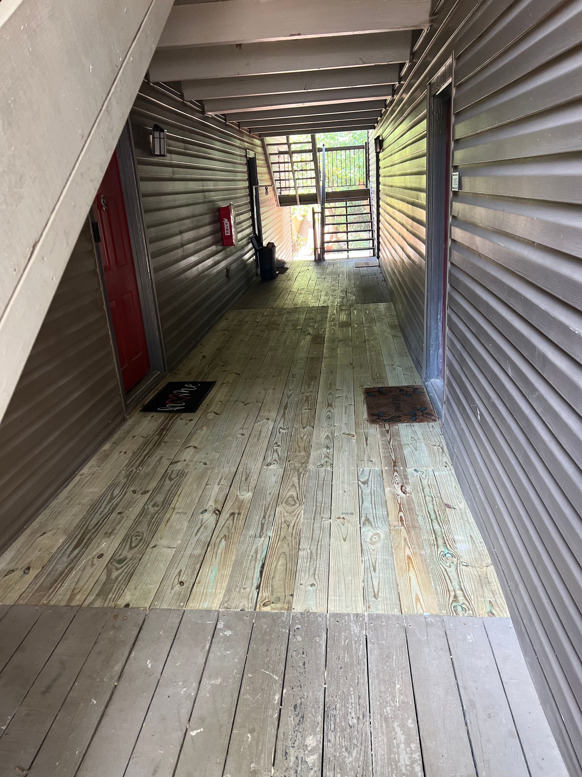 Covered outdoor hallway with wooden floor, stairs, and doors.