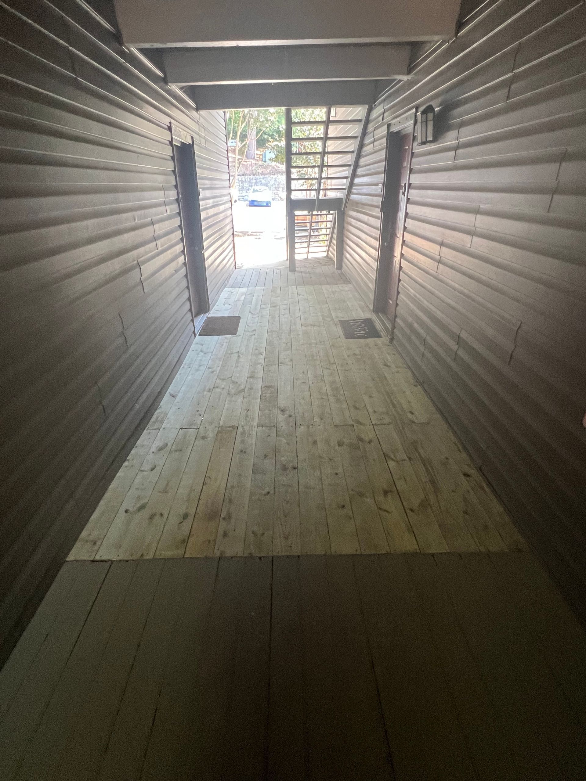 Narrow wooden hallway leading to outdoor light; staircase visible.