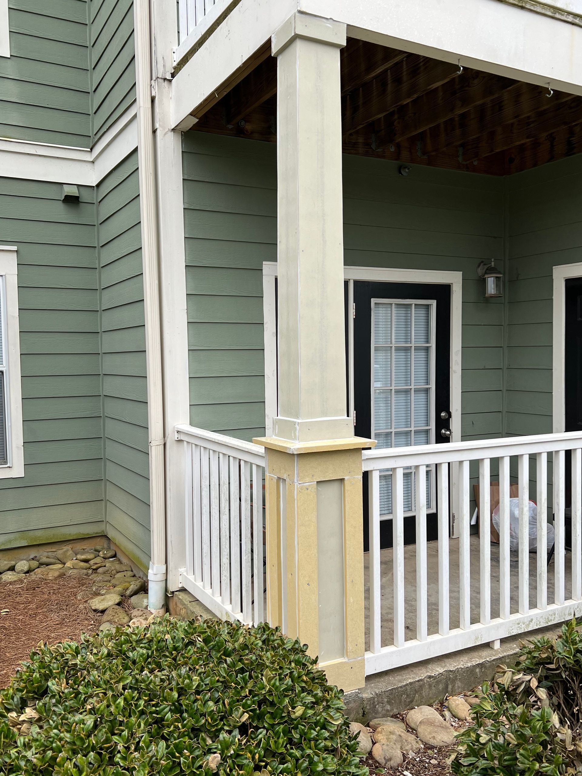 Exterior view of a porch with white railing, light-colored columns, and a green exterior wall.
