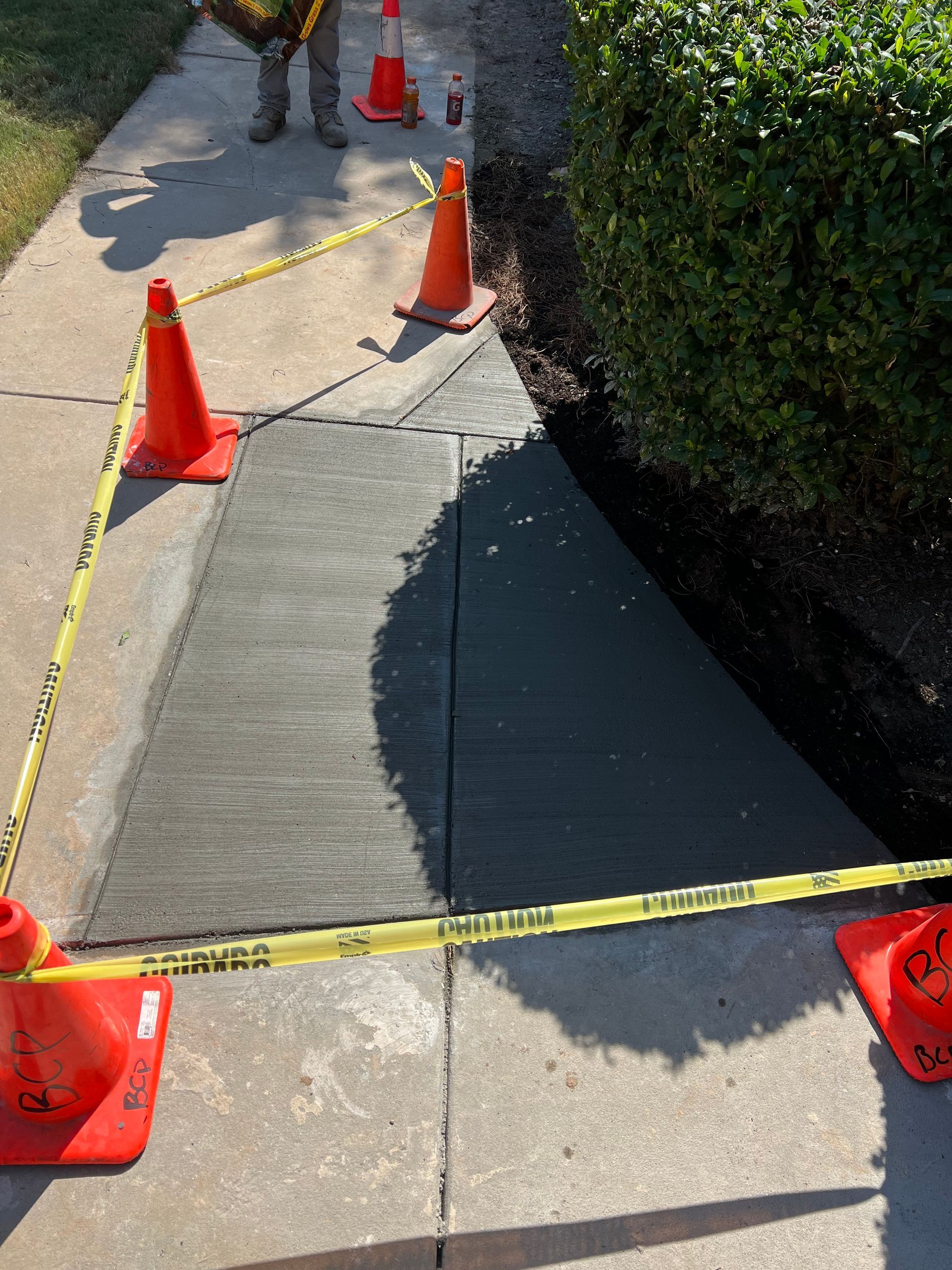 Fresh concrete sidewalk repair with orange cones and caution tape.