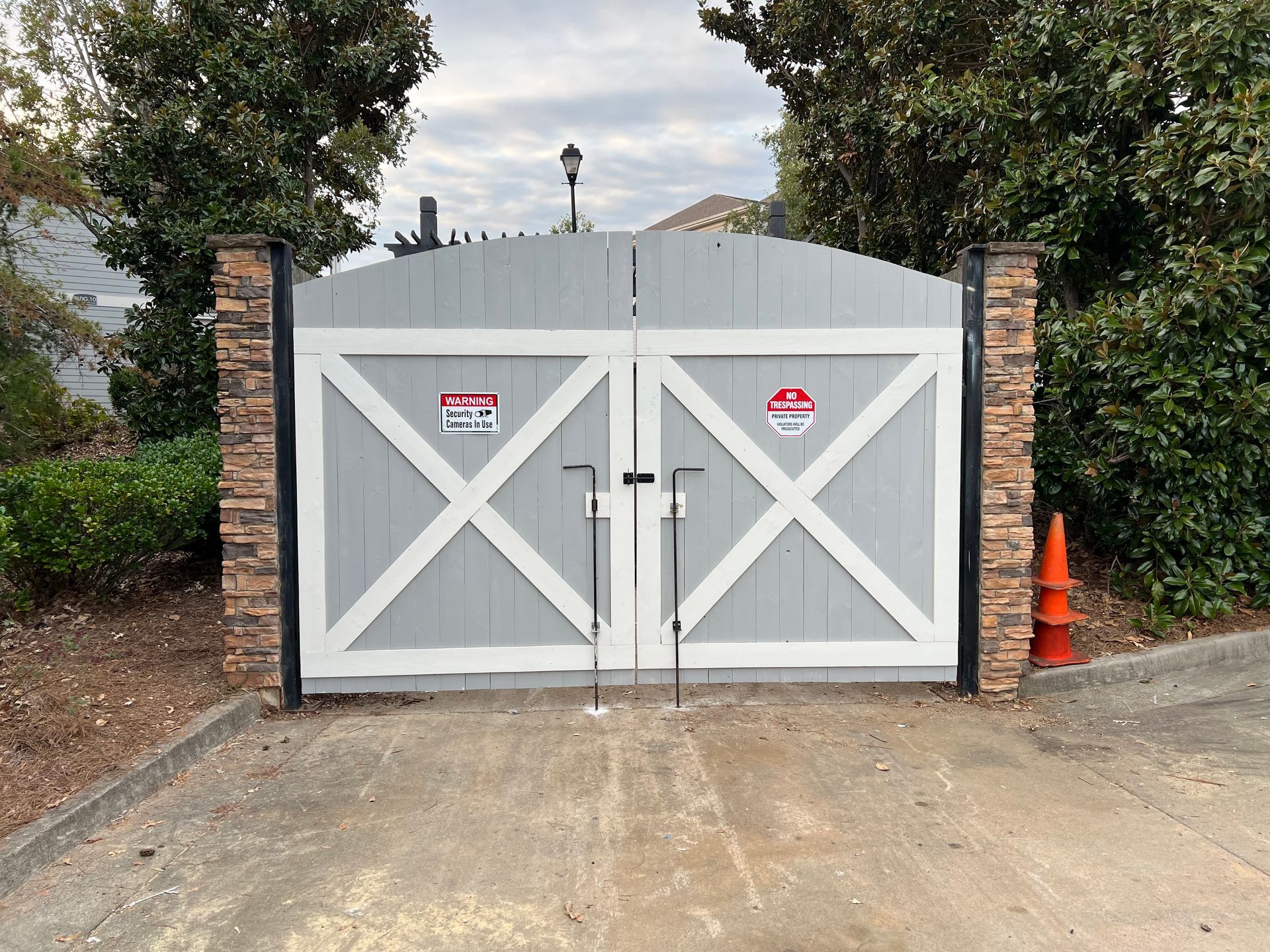 Gray wooden gate with white cross design, brick pillars, and no trespassing signs.
