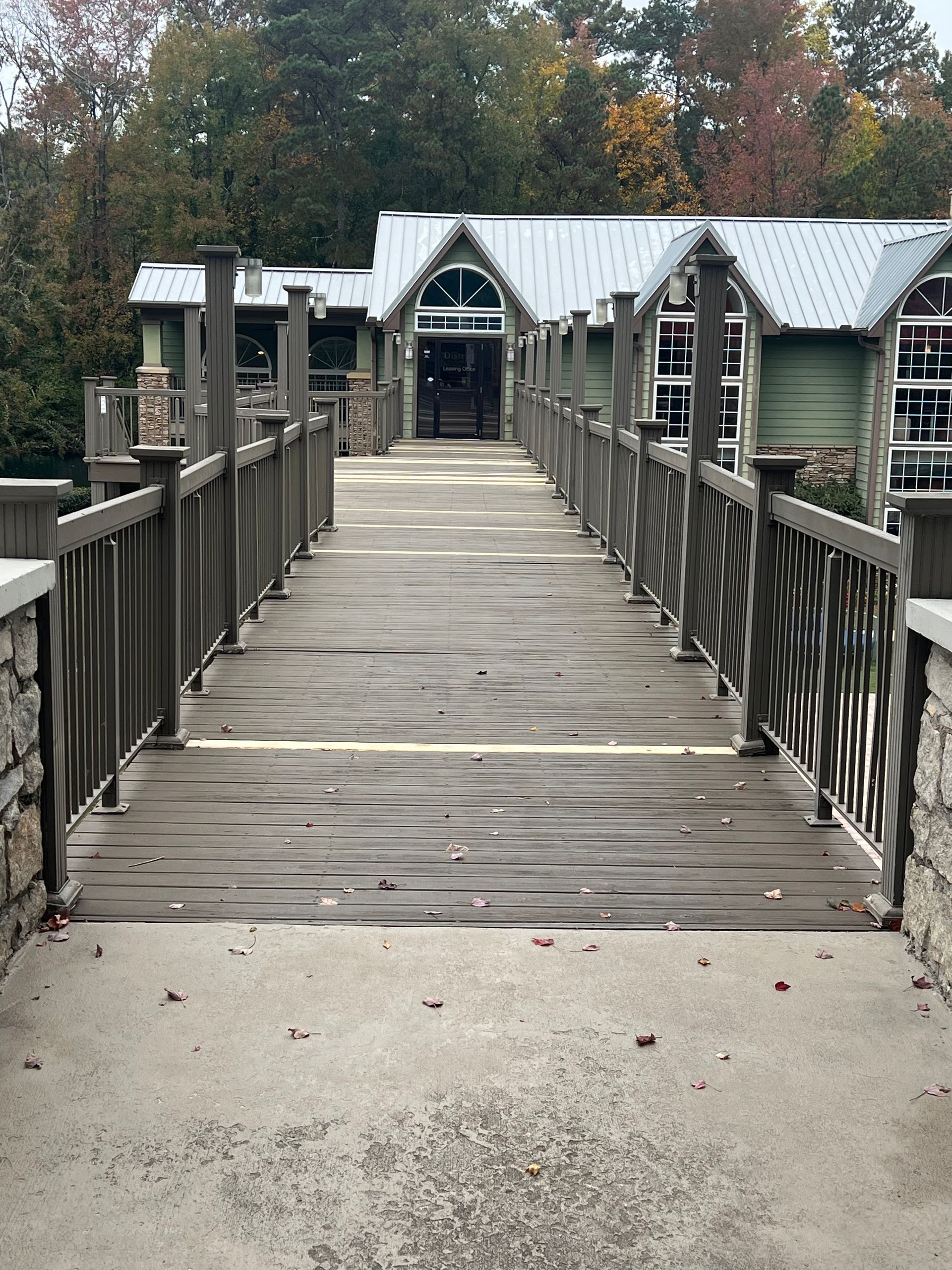 Wooden bridge leading to a green building with a metal roof. Fall foliage surrounds the area.