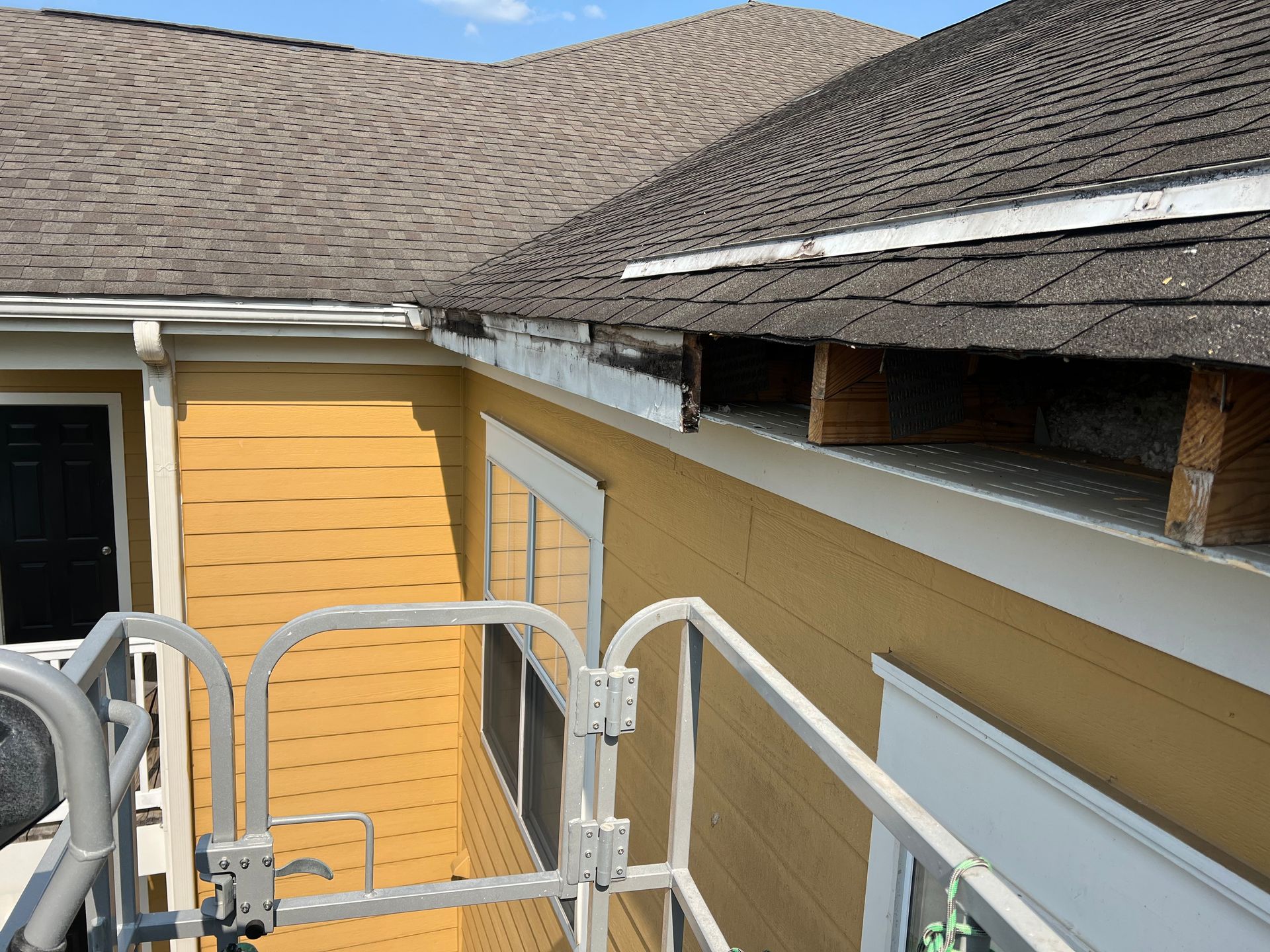 Yellow building exterior with roof damage, showing exposed wood and a gutter.