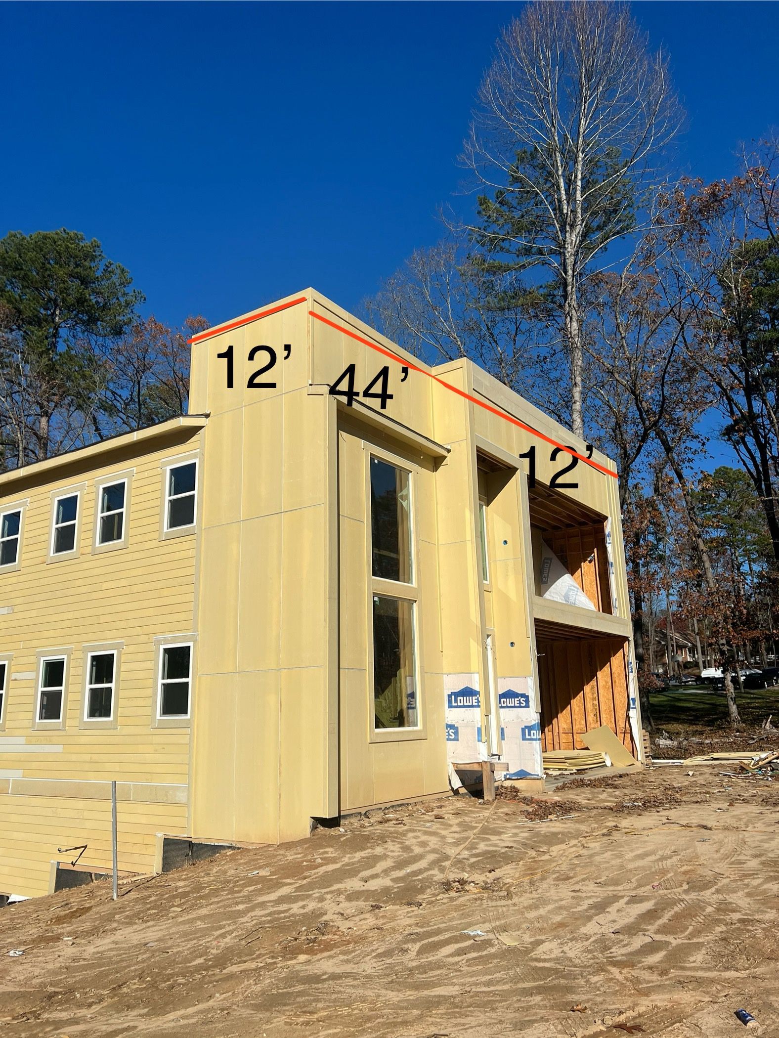Two-story house under construction with exposed wood frame and large windows.  Measurements of 12' and 44' are indicated in red.