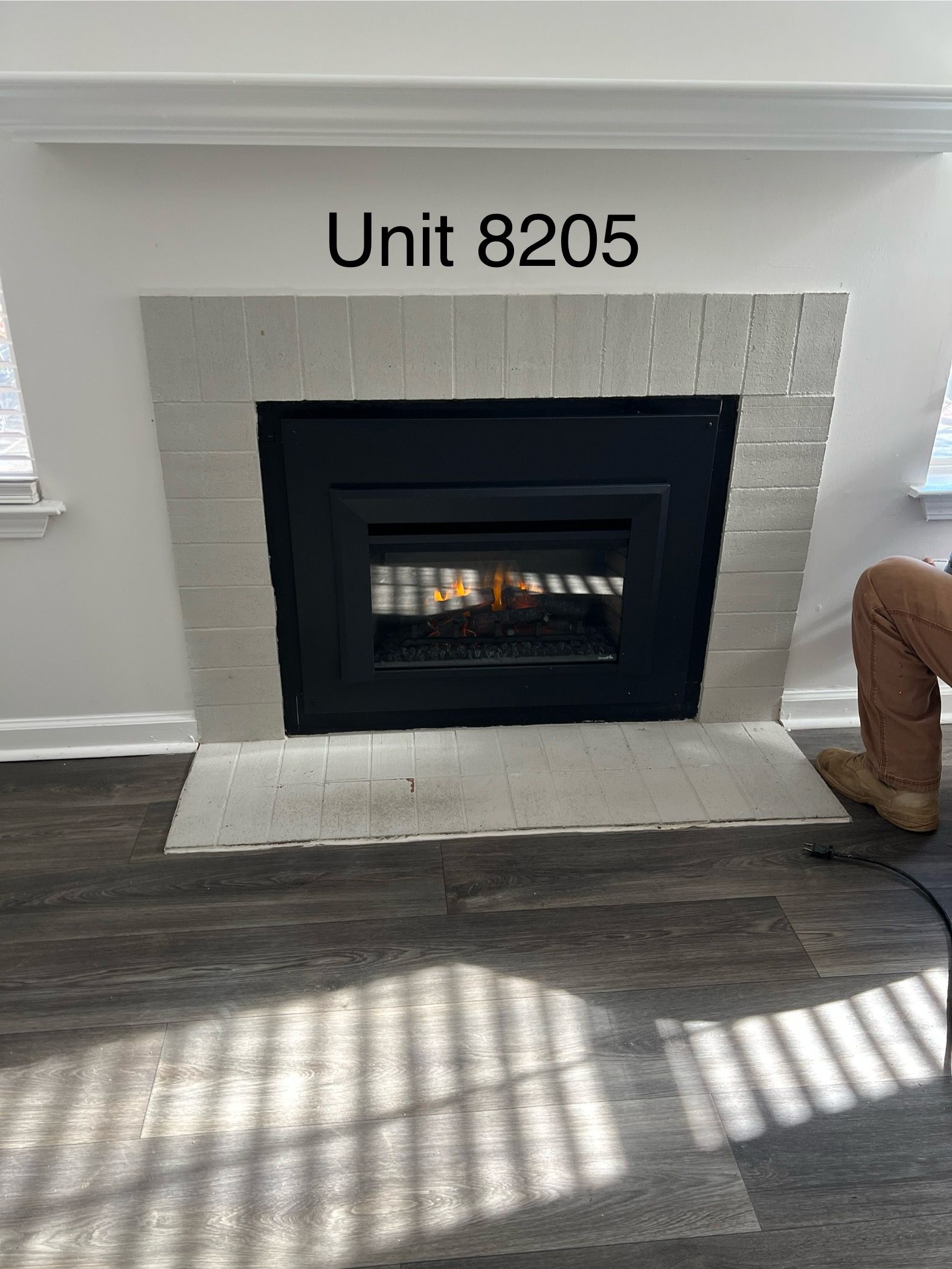 Fireplace in Unit 8205 with white brick surround and black interior. A person's leg is visible on the right.