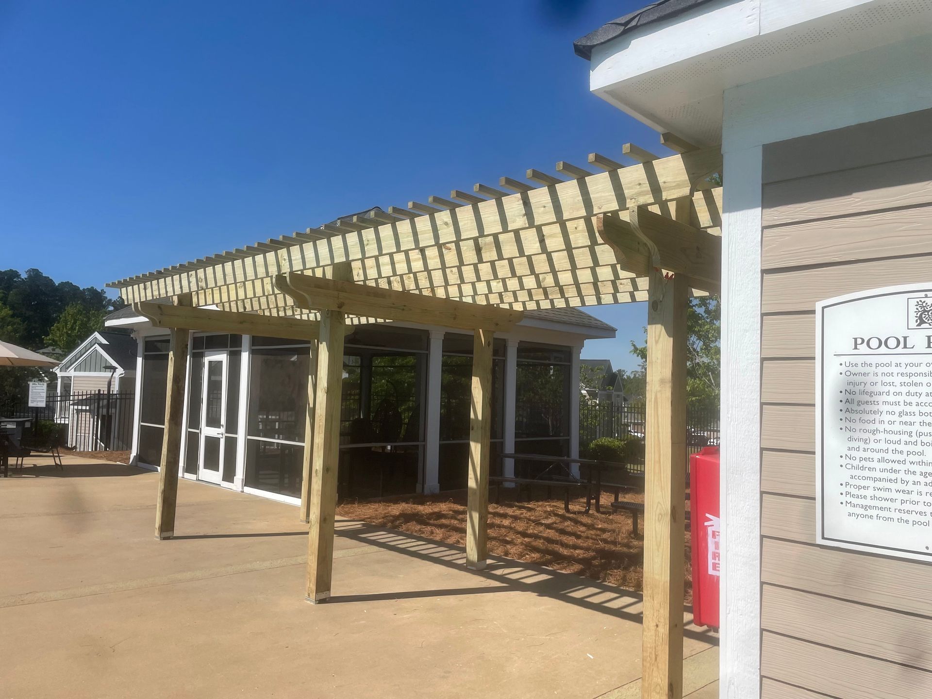 Wooden pergola covering a poolside structure; clear blue sky above.