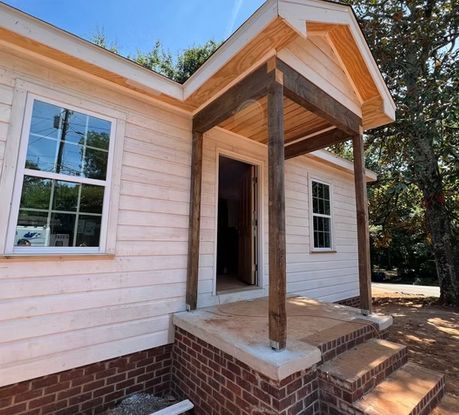 Newly constructed house with porch, brick foundation, and wooden support beams.