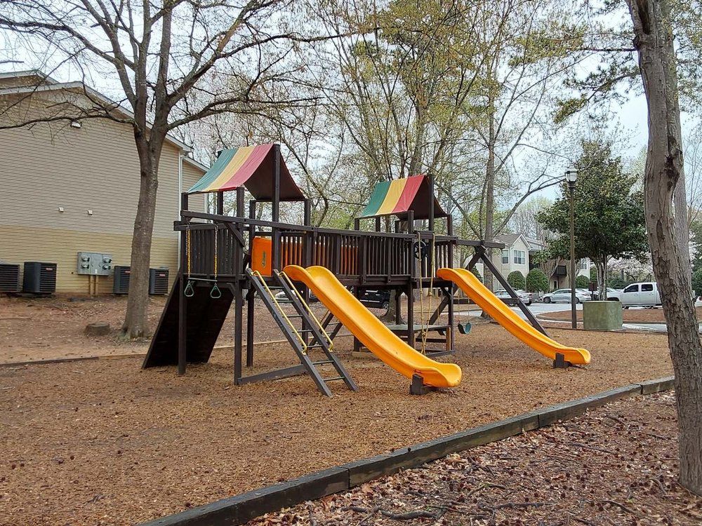 Playground structure with two yellow slides and brown mulch.