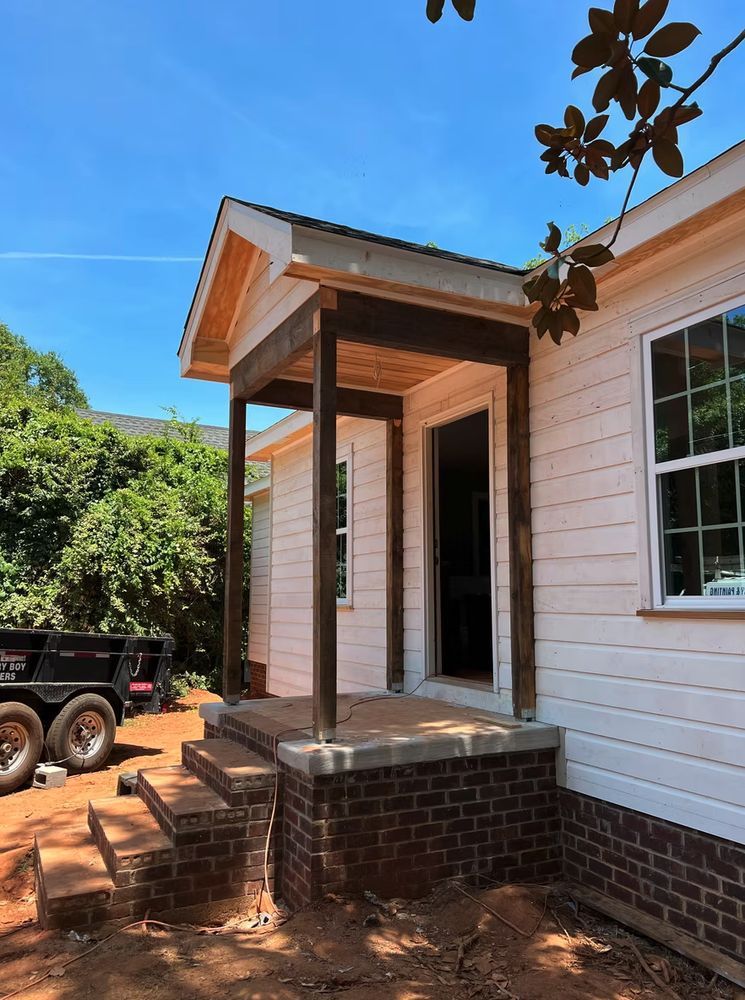 Woman in straw hat smiles, holding wine glass near a lake.