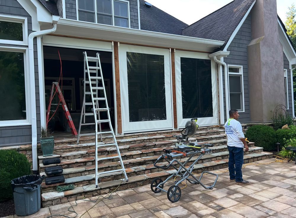 Workers installing outdoor shades on a house porch. Ladders and saw are present.