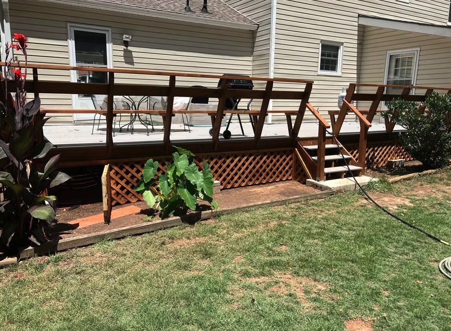 Wooden deck with stairs, lattice skirting, and railing in a backyard with green grass.