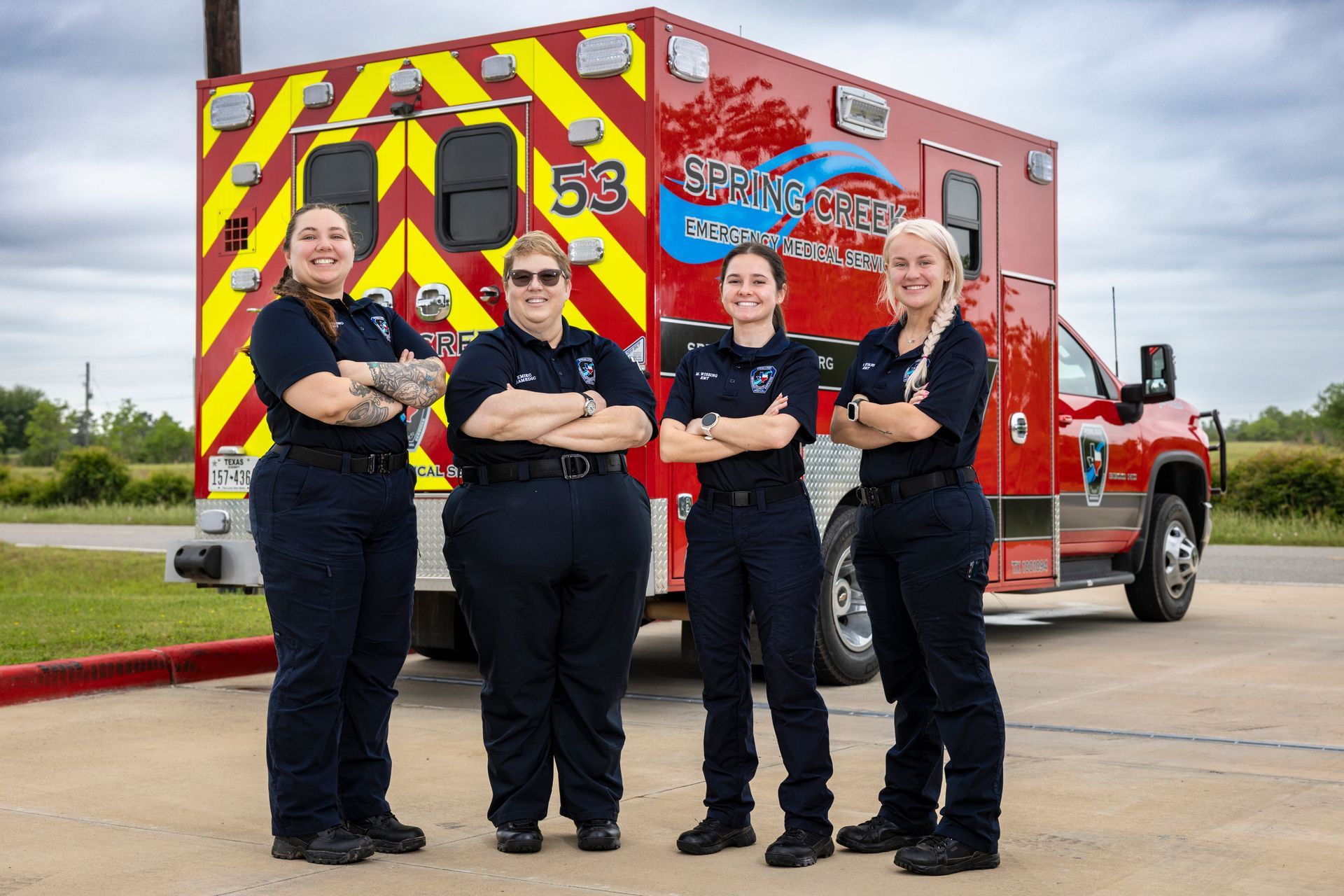 Four firefighters standing in front of a red fire truck with yellow-striped rear doors
