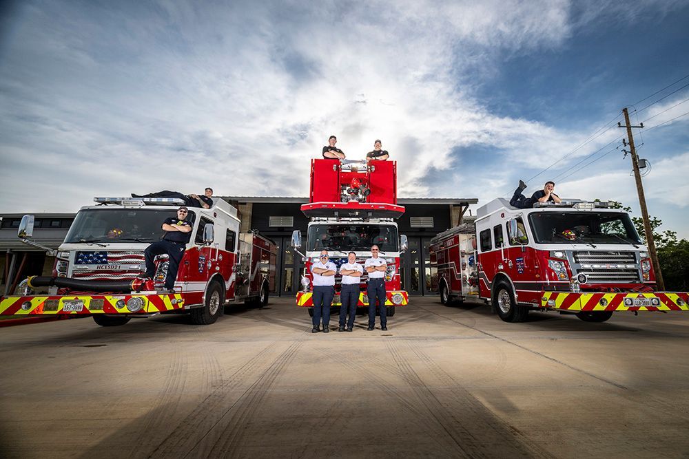 Fire trucks and firefighters lined up in front of a station under a cloudy sky