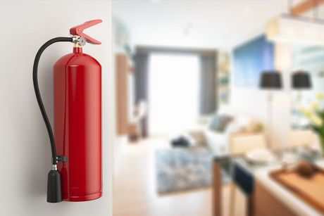 Red fire extinguisher mounted on a wall in a blurred living room.