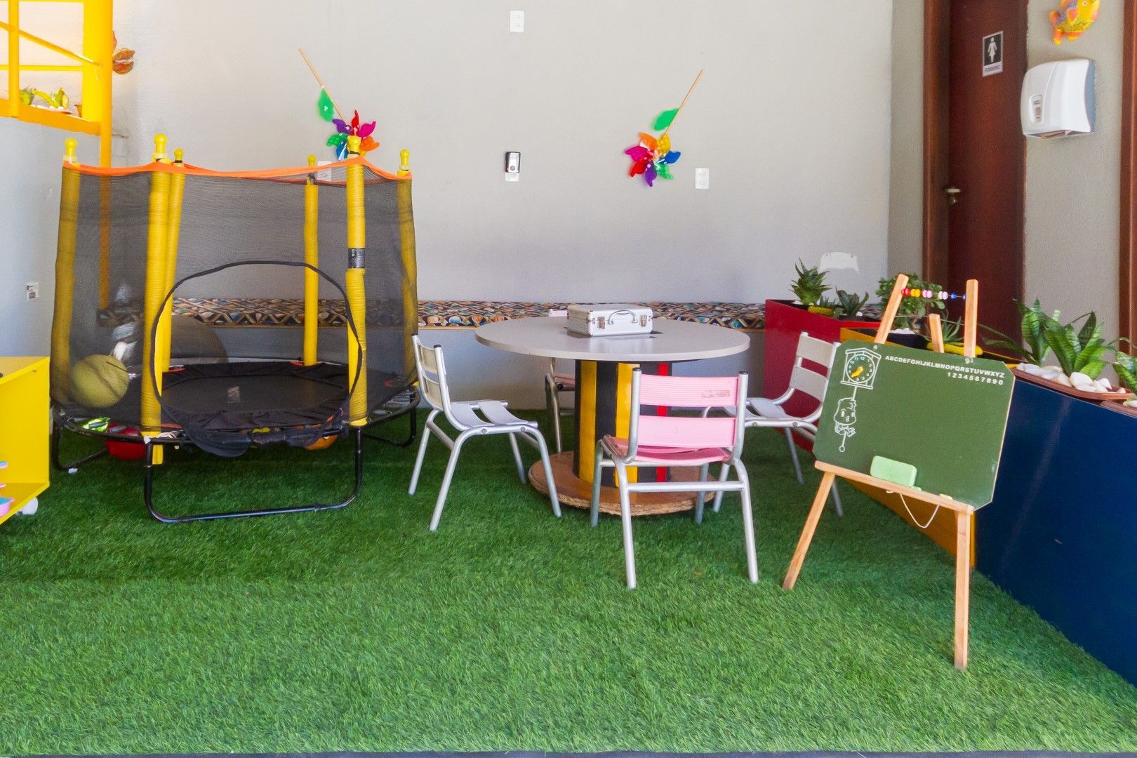 Uma sala com uma mesa, cadeiras, um trampolim e um quadro negro.