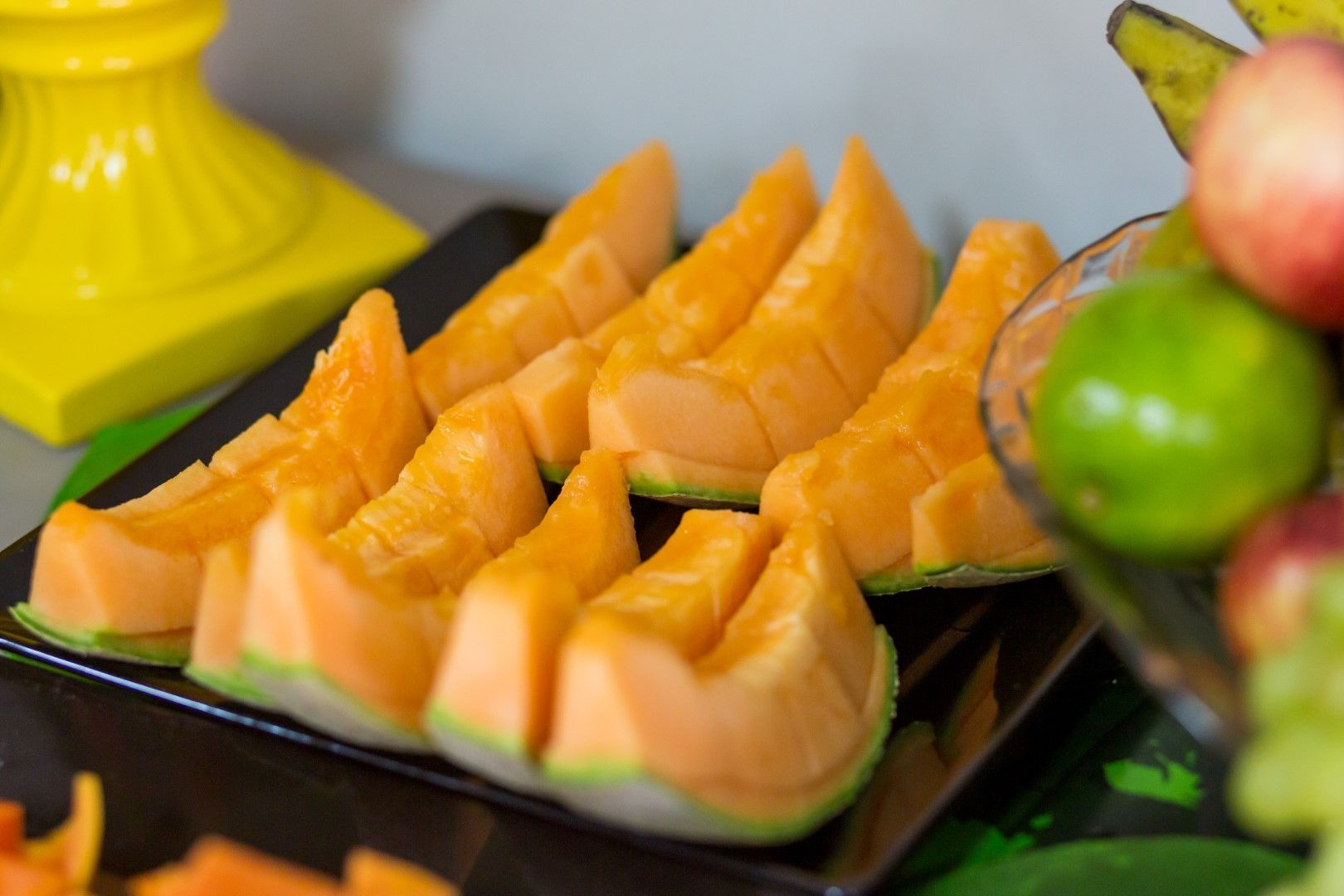 Um prato preto coberto com fatias de melão ao lado de uma tigela de frutas.