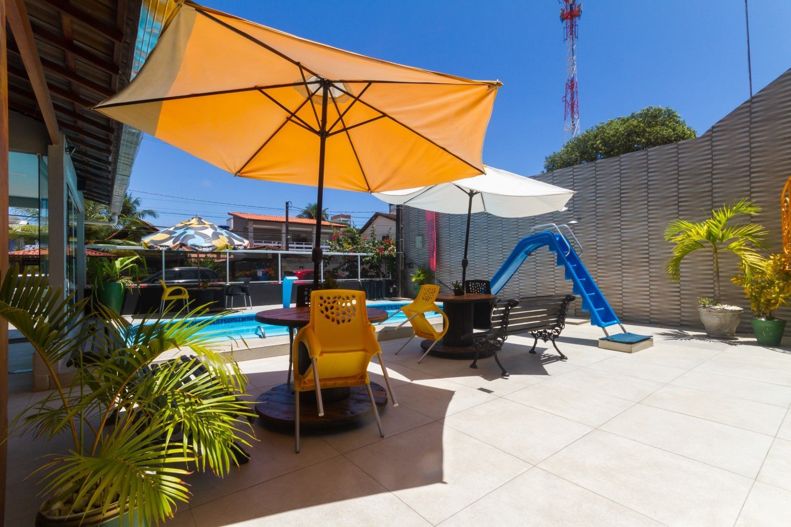 Um guarda-chuva amarelo está em um pátio próximo a uma piscina.