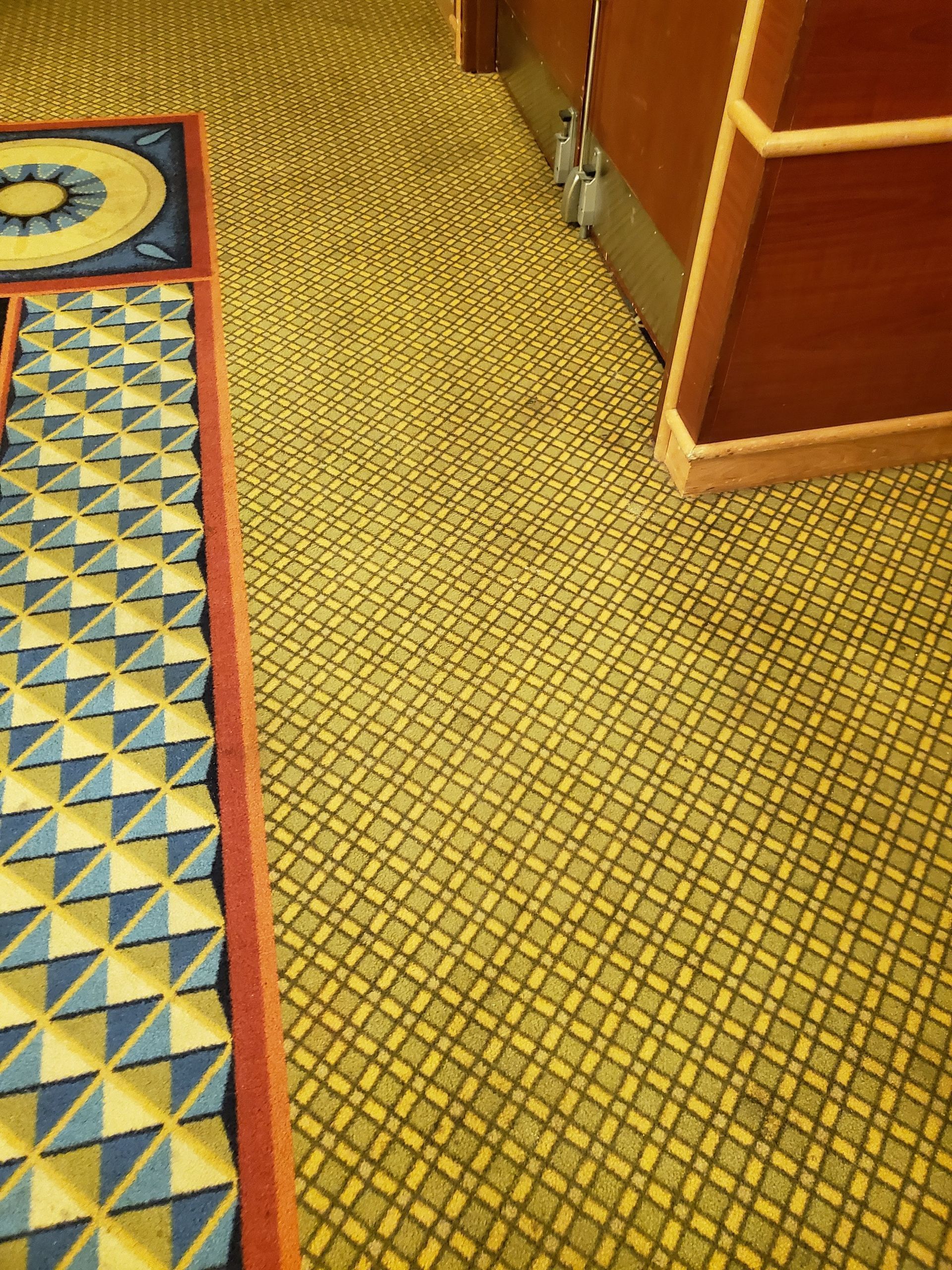 A patterned carpet featuring yellow-green cross-hatching and a decorative border with blue and yellow geometric shapes.