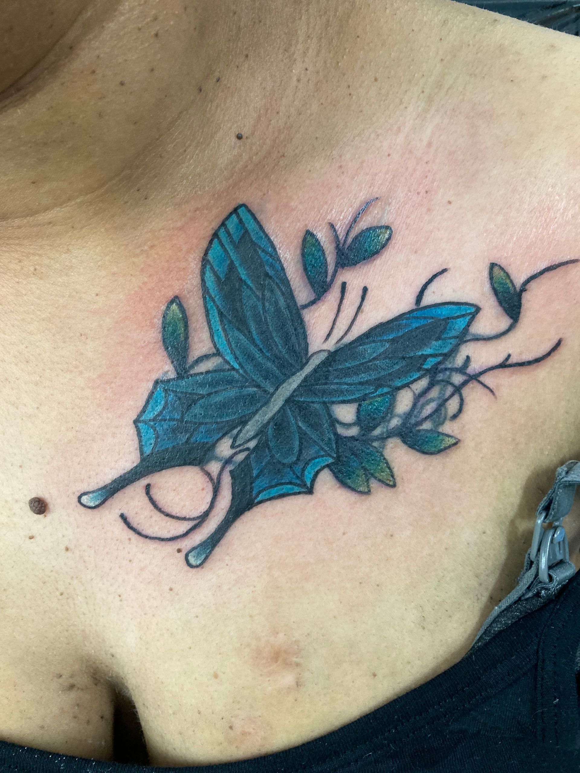 A Woman Has a Blue Butterfly Tattoo on Her Chest — La Bomba Loca Tattoo in Cairns City, QLD