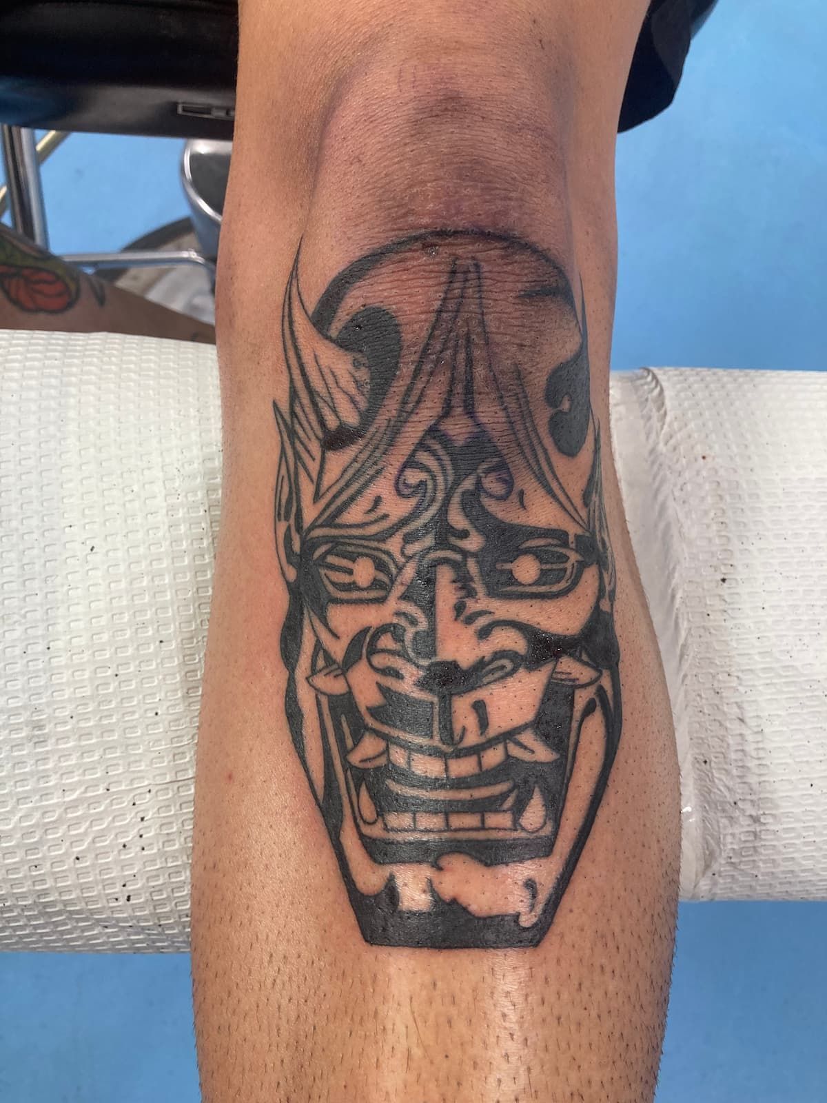 A Person Has a Tattoo of a Demon Mask on Their Leg — La Bomba Loca Tattoo in Cairns City, QLD