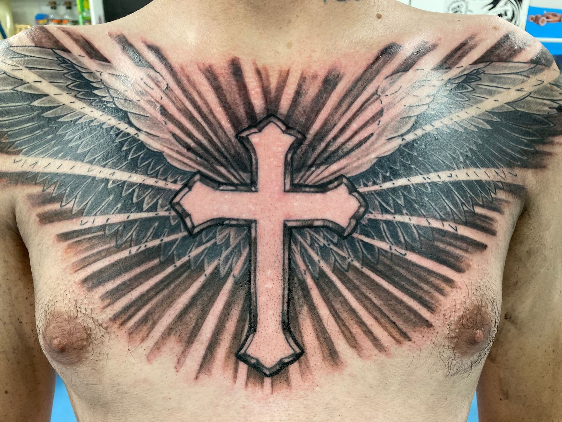 A Man Has a Tattoo of a Cross and Wings on His Chest — La Bomba Loca Tattoo in Cairns City, QLD