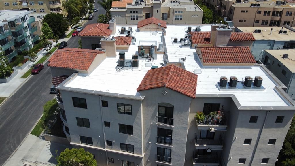 Aerial view of a multi-story building with a white flat roof and red tile accents.