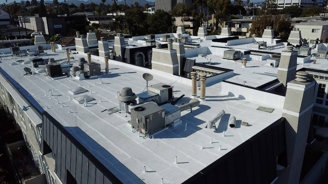 Rooftop of a building with various equipment and ventilation structures. White roof, with city and trees in the background.
