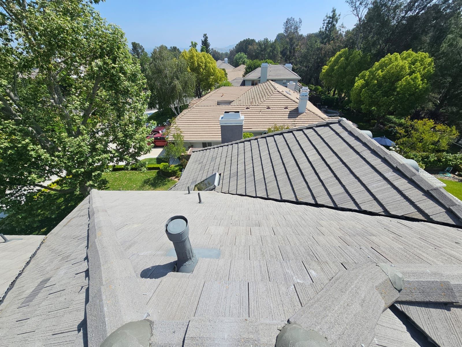 View from a roof overlooking a neighborhood with trees and houses under a bright blue sky.