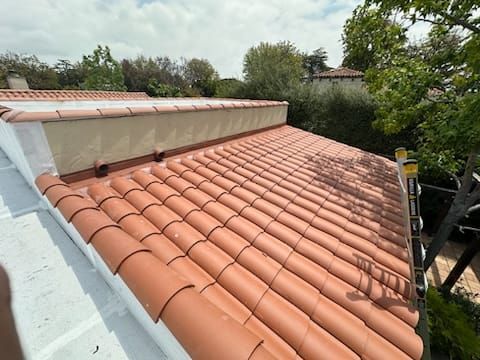 Red tile roof on a building with a white wall next to foliage.