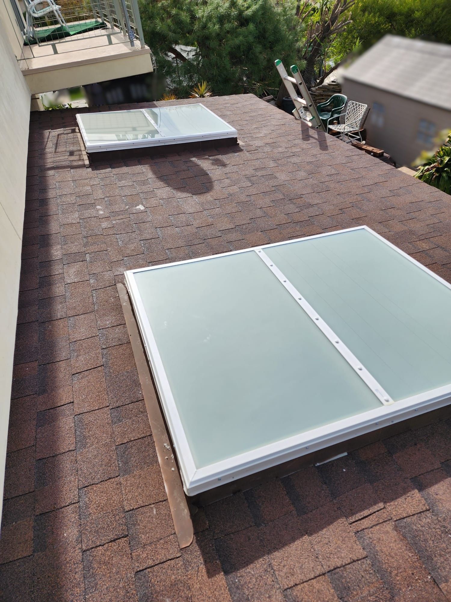 Two skylights on a brown shingle roof. A ladder and balcony are visible nearby.