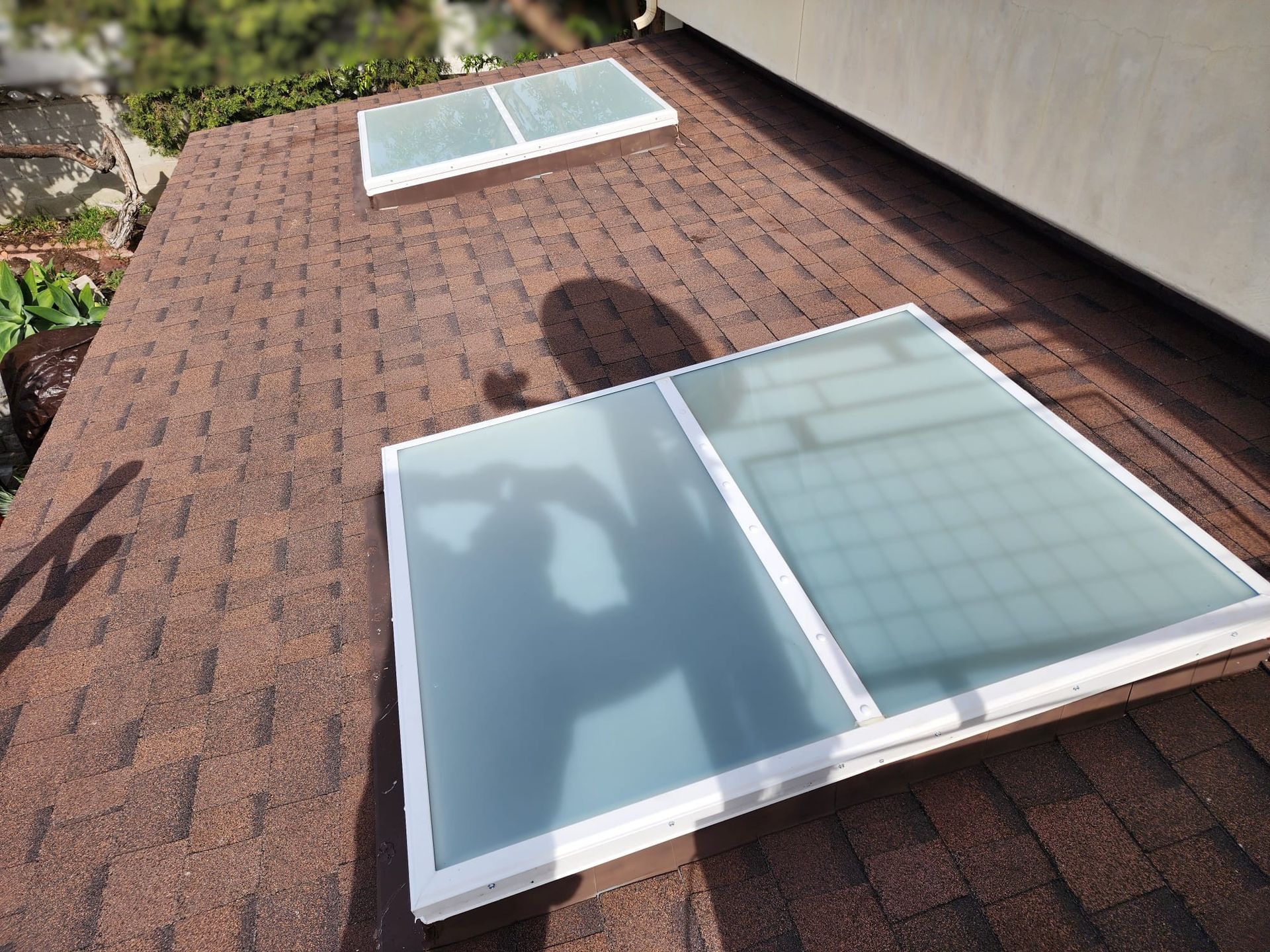 Two skylights on a brown shingle roof, casting shadows.