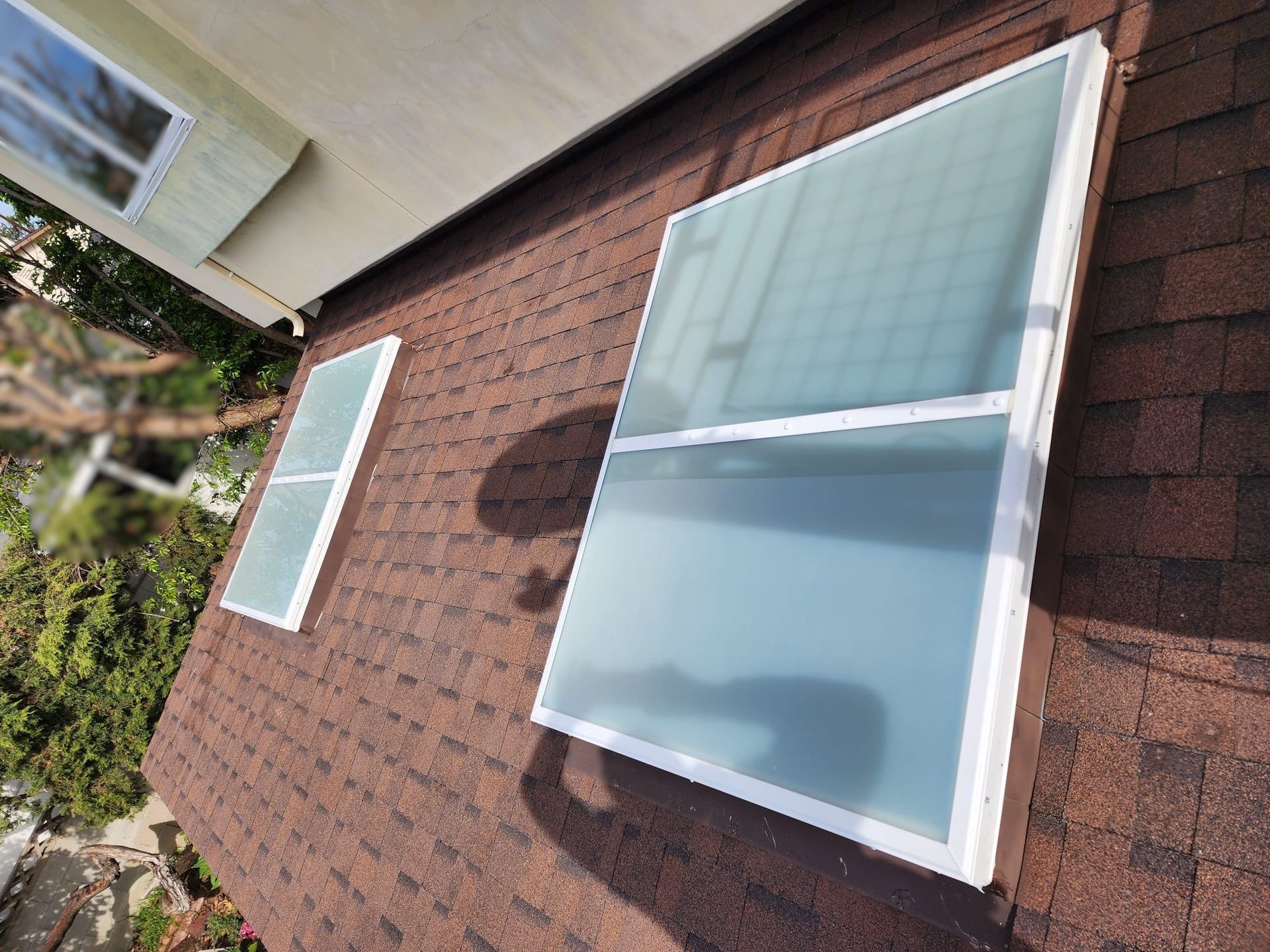 Two white-framed skylights on a brown shingled roof. One is tall, divided, the other is smaller.
