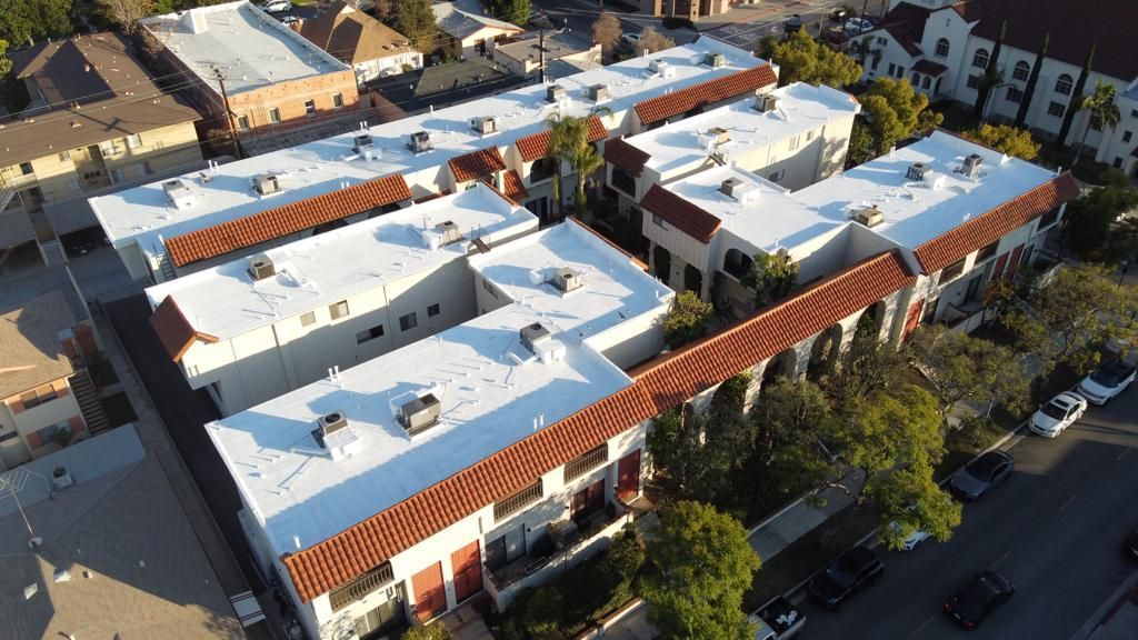 Aerial view of a cream-colored apartment complex with red-tiled roofs in a sunny residential area.