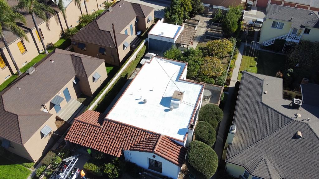 Overhead view of houses with brown and white roofs, green trees and bushes.